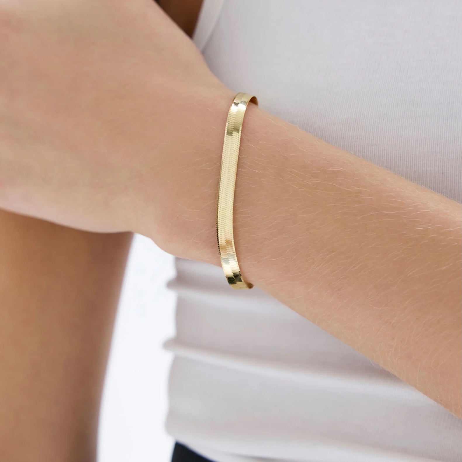 Bracciale rigido dorato a fascia indossato.